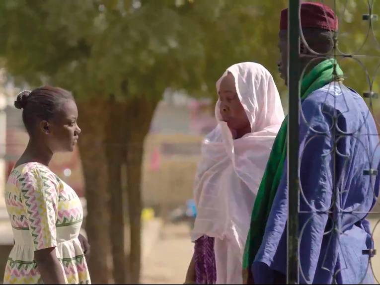 Eine junge schwarze Frau steht vor zwei älteren Personen.